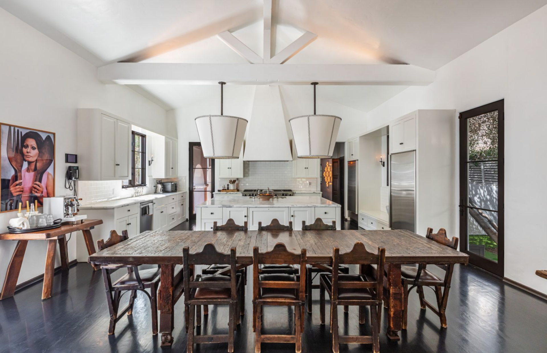 Just off the island, the dining area consists of a long, weathered wood table with matching chairs, positioned to keep it directly connected to both the kitchen and the lounge. 