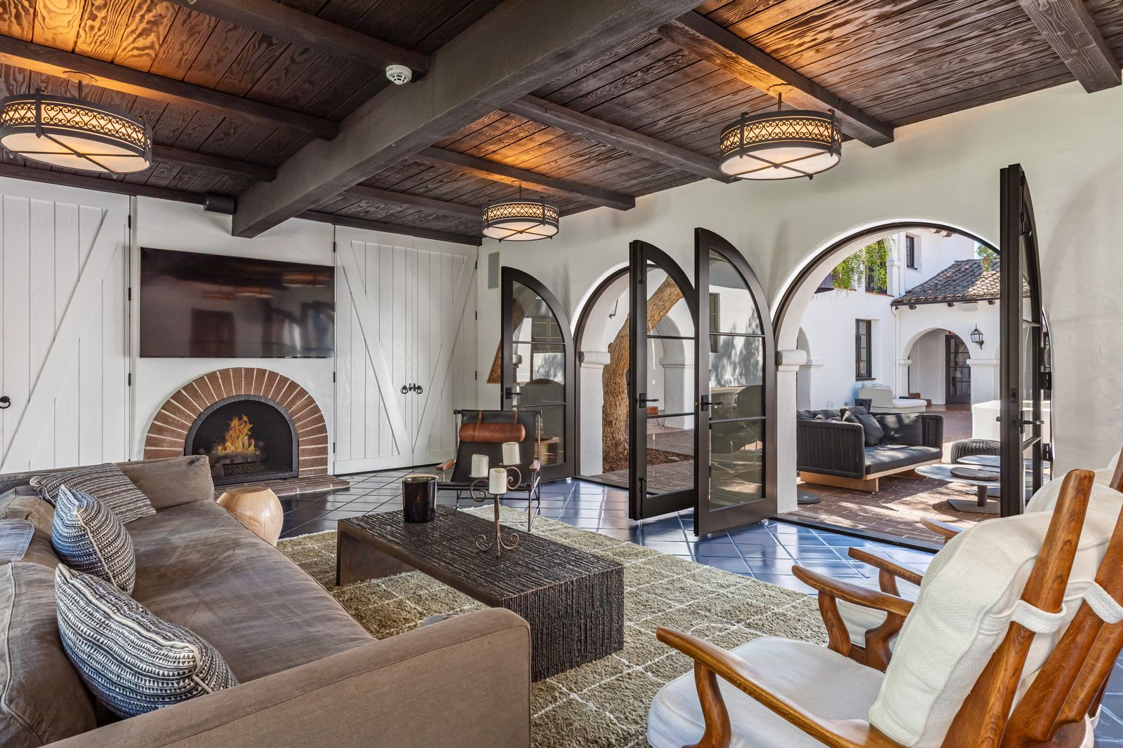 The media room connects directly to the courtyard through arched French doors, while a brick-lined fireplace sits beneath the mounted TV.