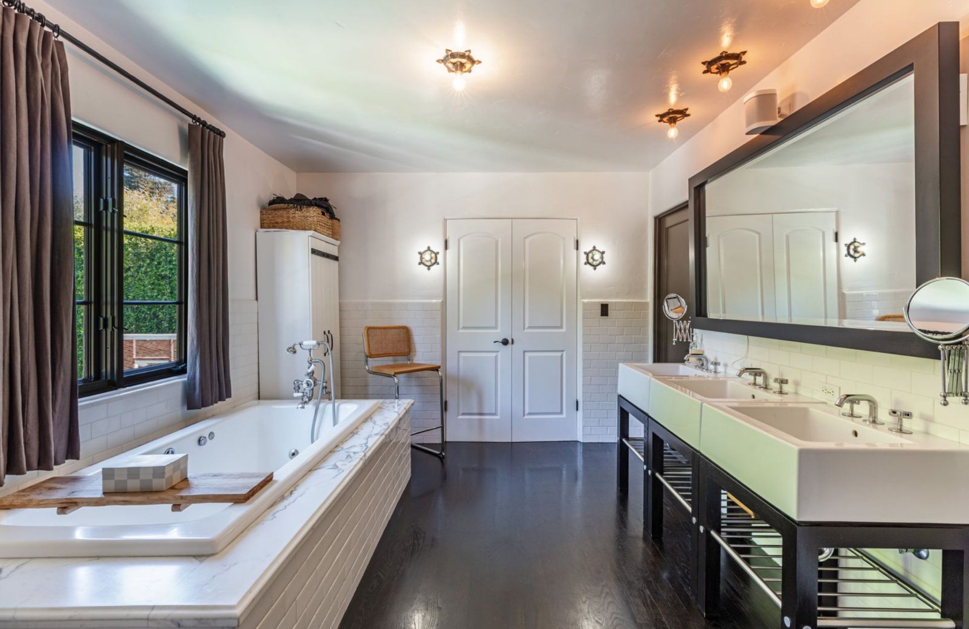 Just beyond the bedroom, the first bathroom is organized with a marble soaking tub set beneath a window on one side and a long double vanity running along the opposite wall.