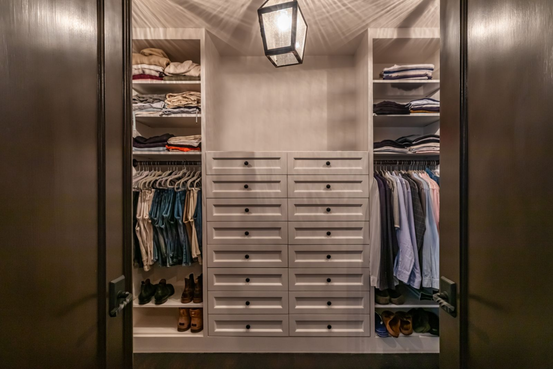 The walk-in closet is accessed through paneled doors and is arranged with built-in shelving and hanging space on both sides. 