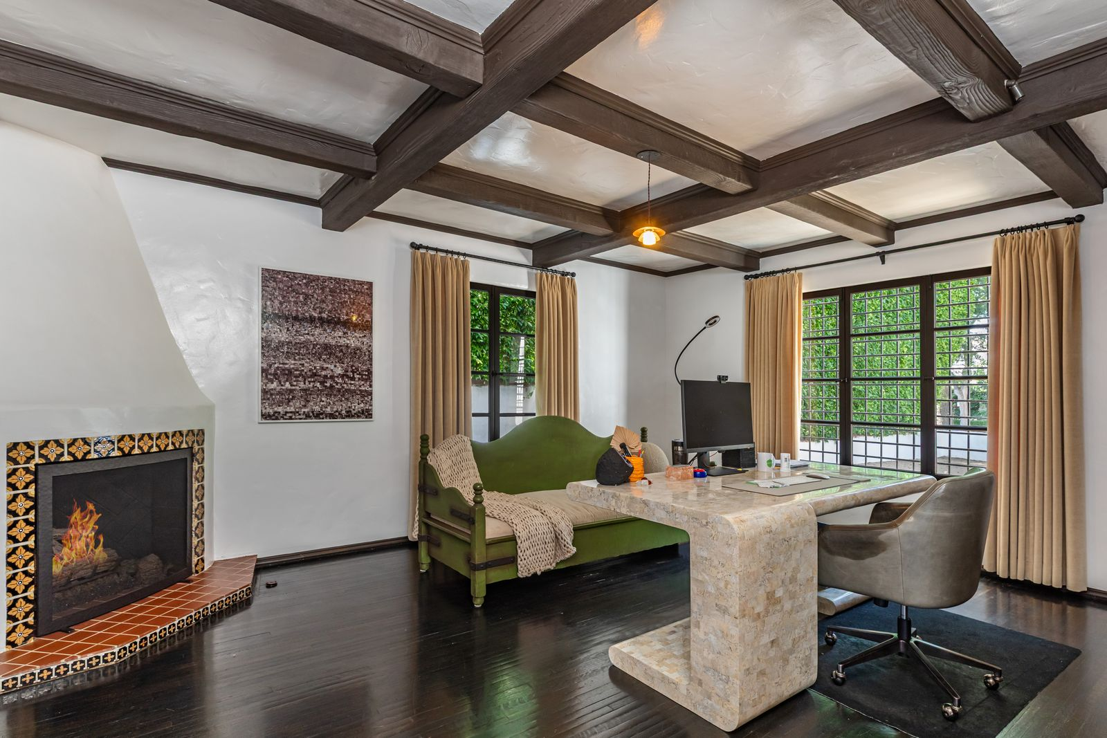 The office has a tiled fireplace with patterned ceramic detailing and a terracotta hearth, adding color across from the stone desk positioned near the windows.