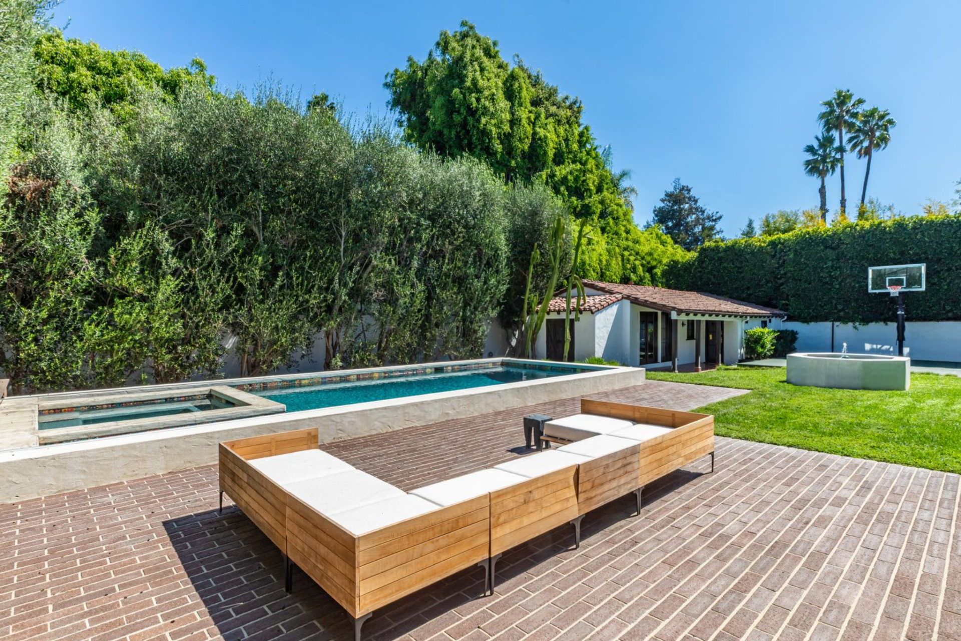 A rectangular pool and spa run along one edge of the yard, bordered by brick hardscaping that connects back to the house. 