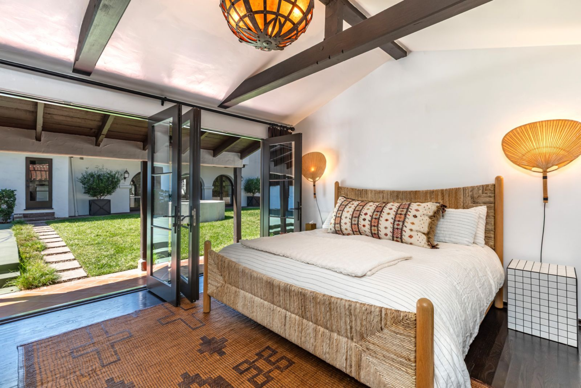 Inside, the bedroom keeps the same Spanish-style design as the main house, with dark wood floors, exposed ceiling beams, and a lantern-style pendant overhead. 