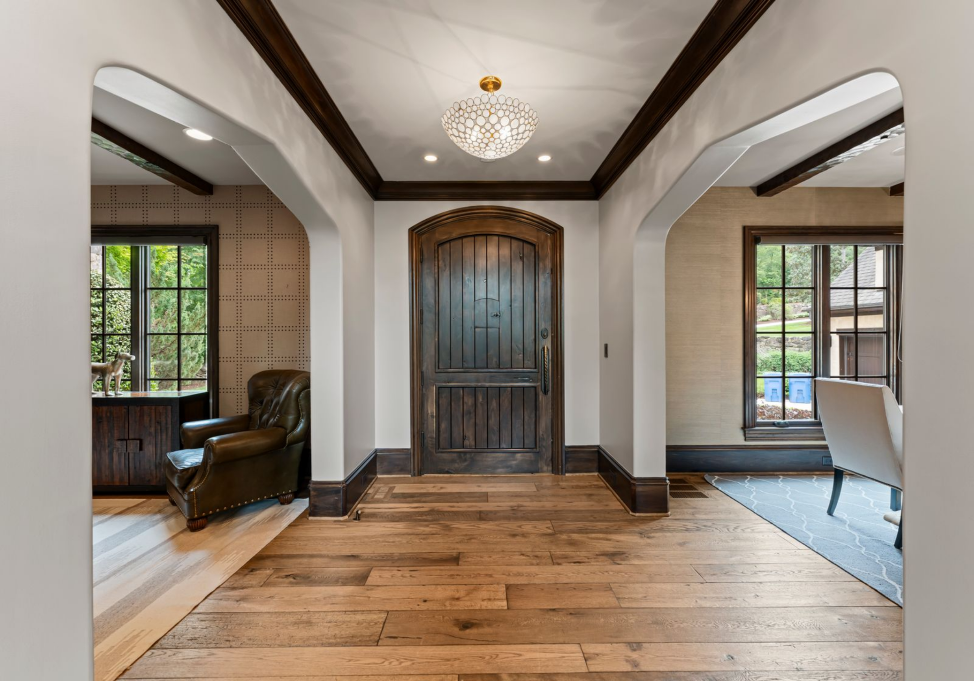 Entering through Martin Truex Jr.'s front door, the first view centers on the foyer itself, where a dark wood, paneled door is framed by clean white walls, recessed lighting, and a statement ceiling fixture.