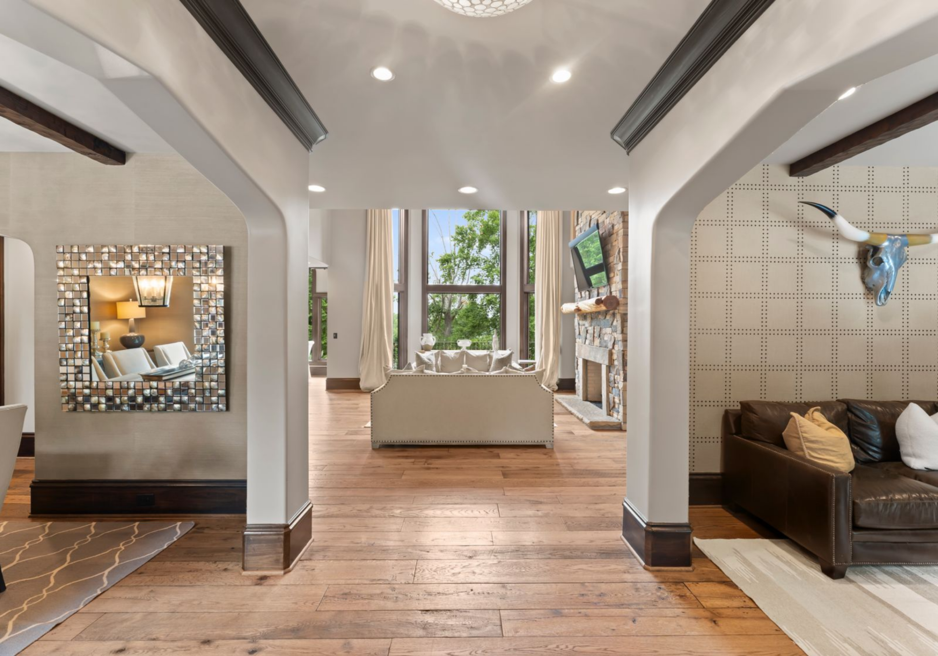 Wide-plank wood floors run underfoot, bordered by darker trim that ties into the door and ceiling accents, while the home's layout opens outward through two symmetrical arched openings.