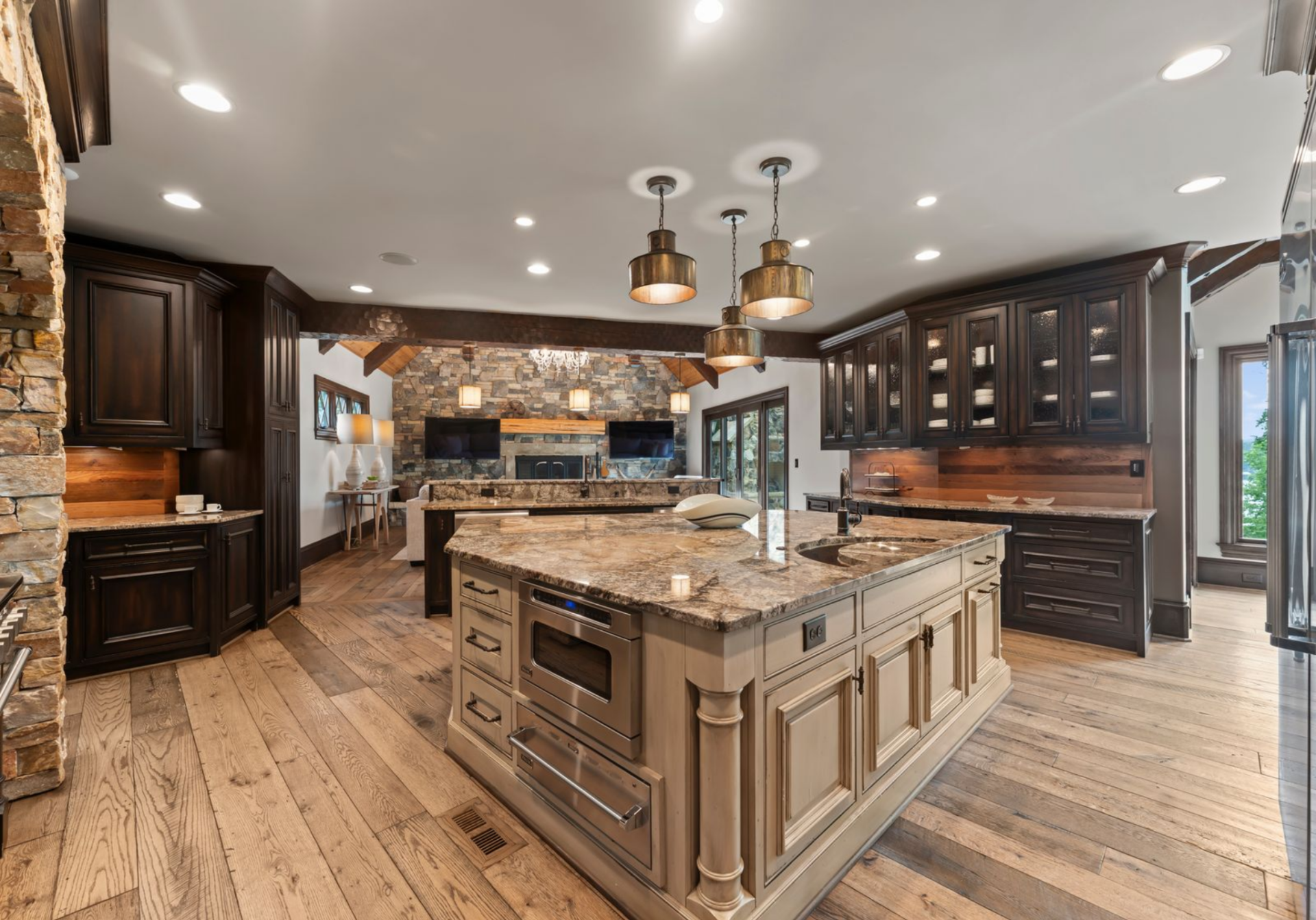 In the center of the space is a large island topped with heavily veined stone and built with storage, a prep sink, and under-counter appliances.