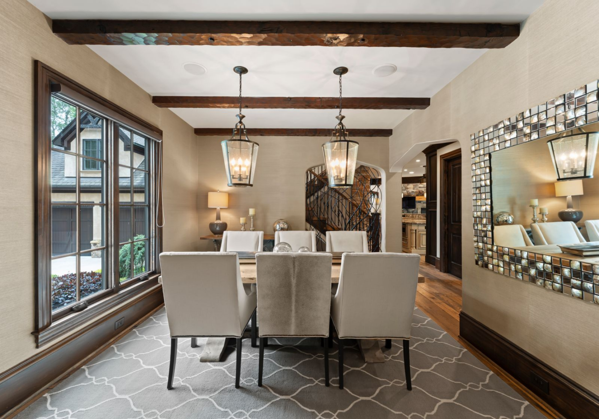 At the front of the house, the formal dining room has a more enclosed layout, with large windows, exposed ceiling beams, and lantern-style pendants over the table.
