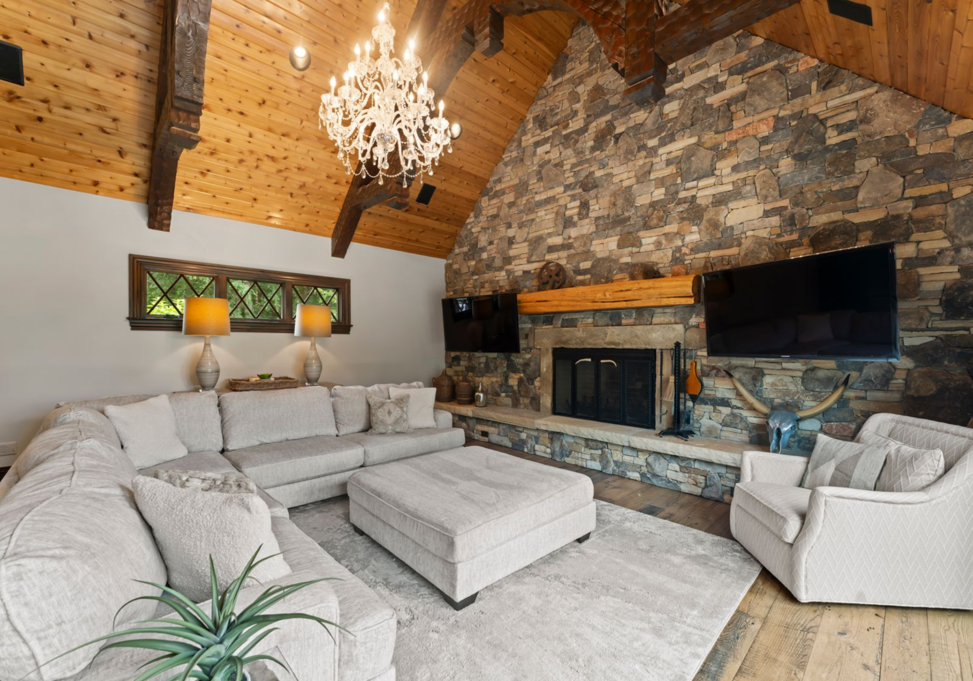 The space features a full-height stone fireplace wall, with a heavy wood mantel, mounted TVs, and a deep hearth running along the base.