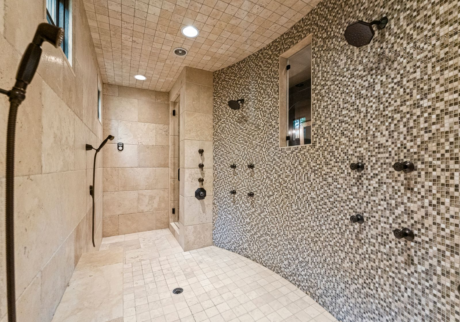 Beyond the soaking tub, the bathroom continues into a large walk-in shower with multiple showerheads, body sprays, and handheld fixtures.