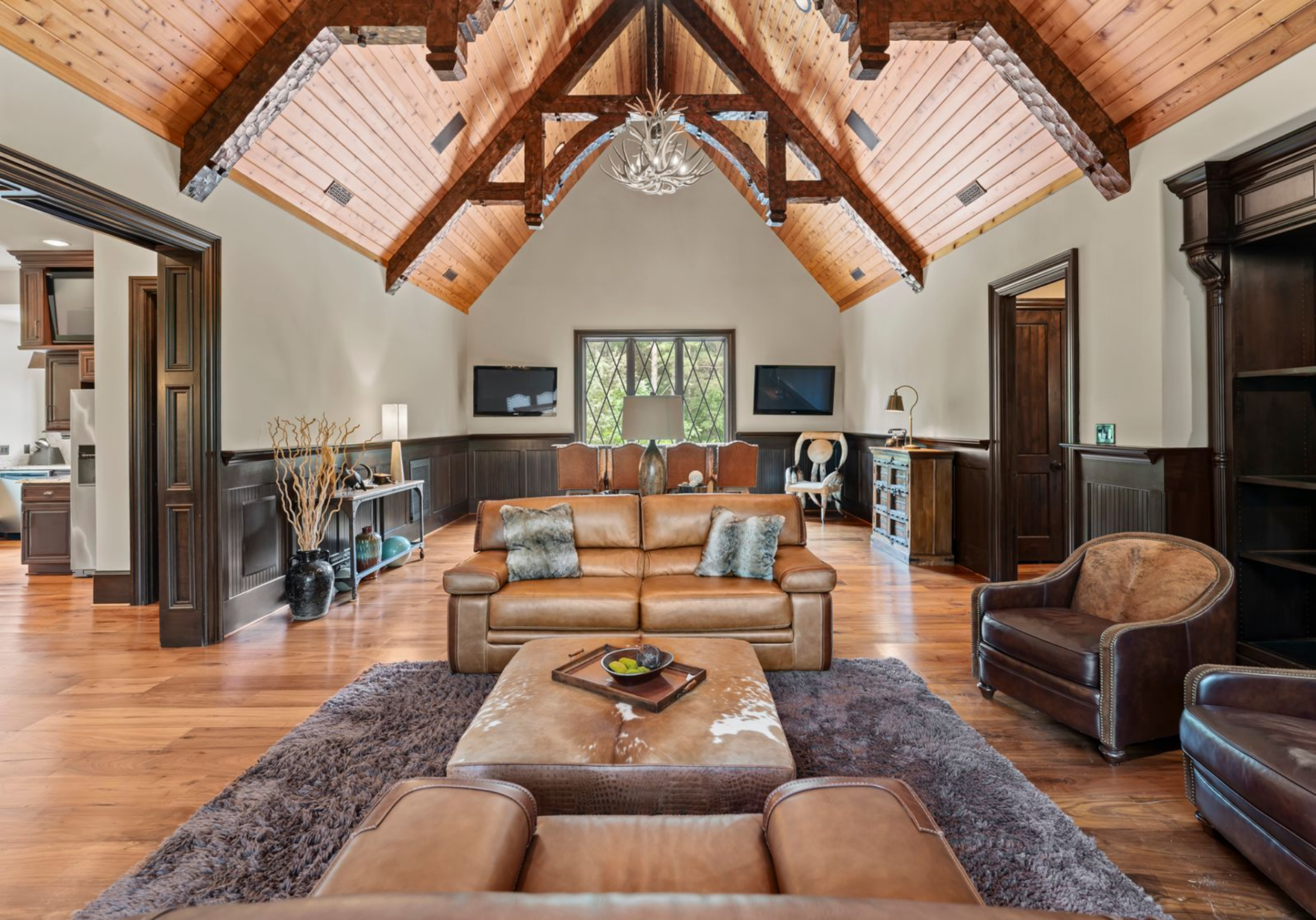 Beyond the kitchen, the living area opens under a vaulted wood ceiling with exposed beams and a leather seating arrangement at the center.