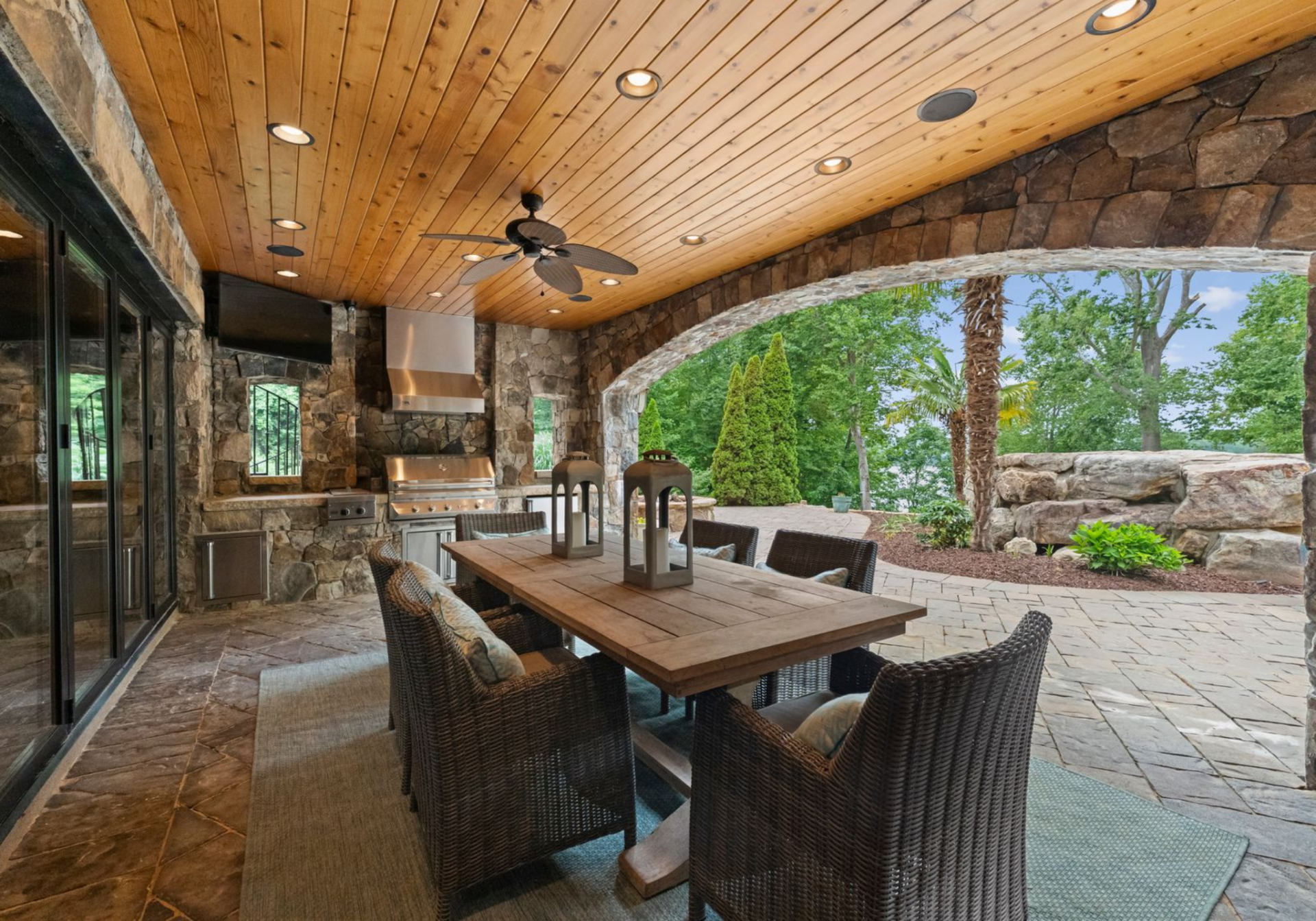 A covered patio sits just off the home, finished with a wood-paneled ceiling, recessed lighting, and a full built-in grilling station set into a stone wall.