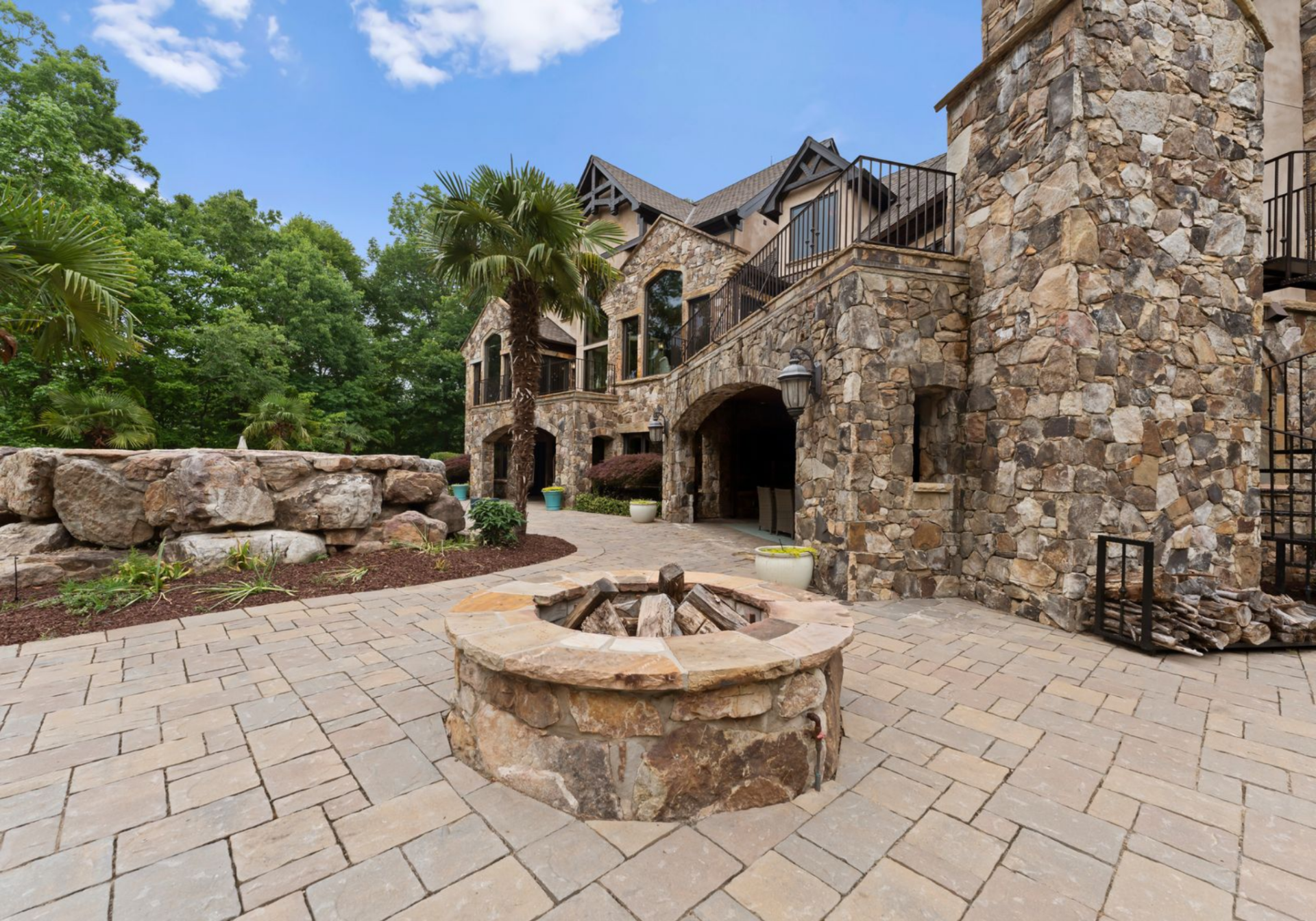 Just beyond the covered area, a circular stone fire pit is set into the paver courtyard, creating a natural gathering point.