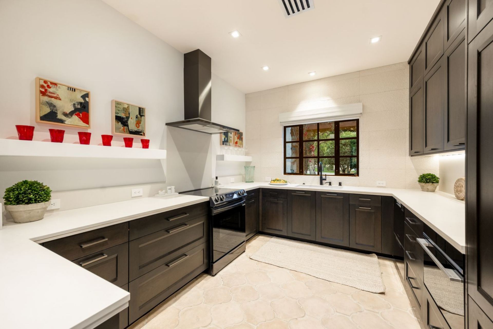 A cooktop, vent hood, wall oven, and broad prep surfaces give the space a functional setup, while the window over the sink brings in light and keeps the room from feeling closed off with its corner placement.