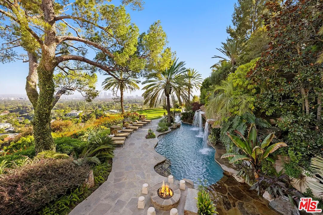 At the corner of the pool, a fire pit is framed by a circle of intricately carved stools, before the stone-tiled patio leads to a section of the pool lined with lounge chairs.