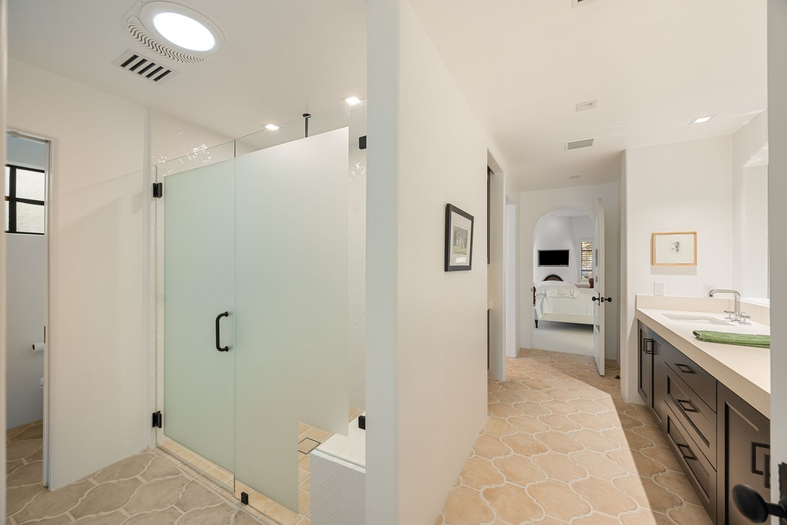 Further in, the layout continues to a glass-enclosed shower and separate water closet, keeping the bath functional while maintaining the same clean, understated design as the bedroom.