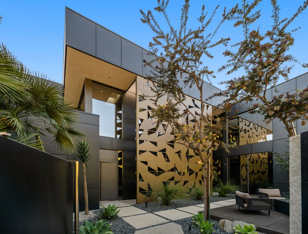 Before even stepping inside the mansion, a geometric gold sculpture rises behind a clean-lined path and front yard patio, where sharp angles and sleek matte finishes contrast against soft landscaping and scattered desert palms.