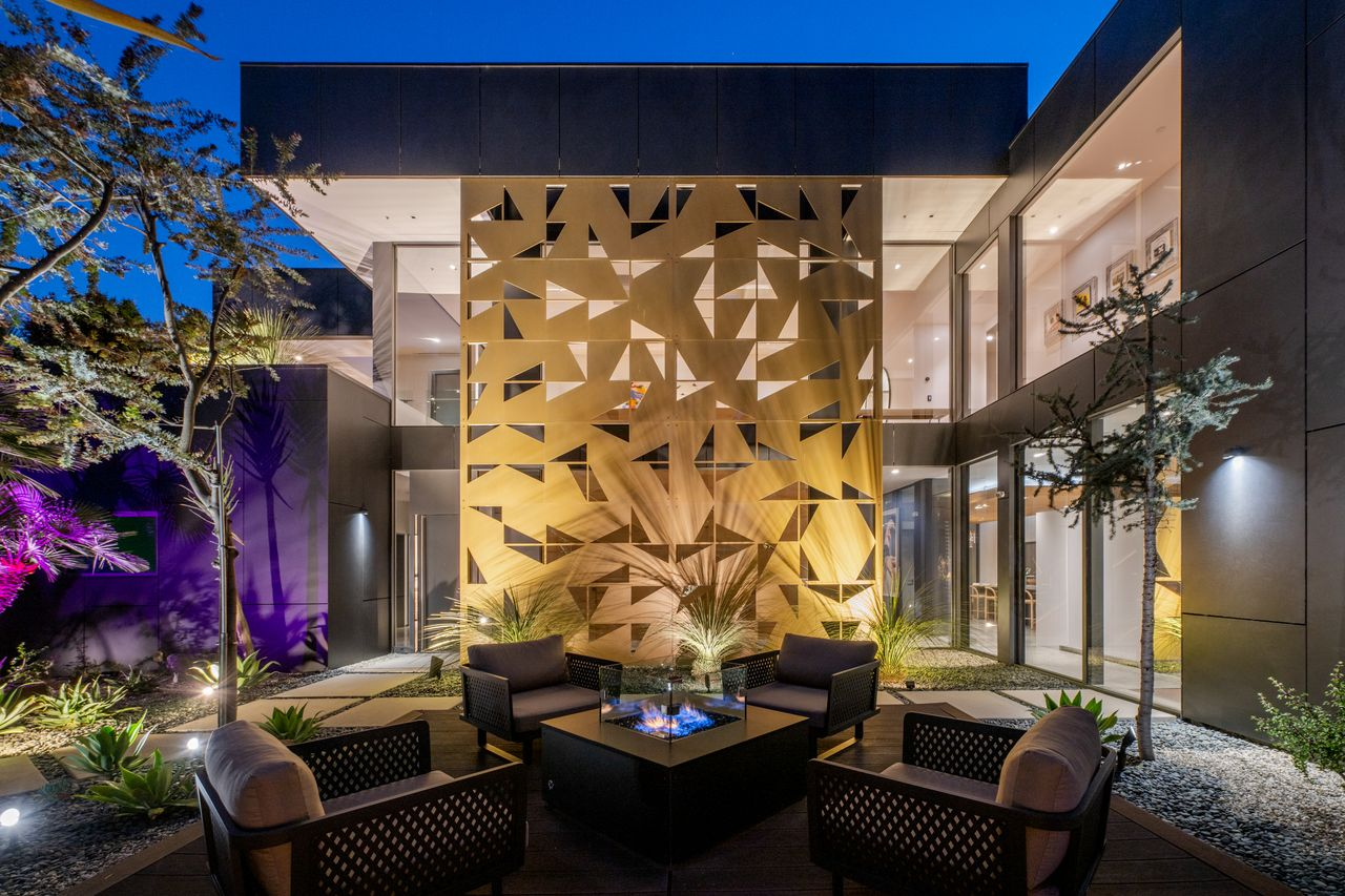 A geometric gold sculpture rises behind a clean-lined path and front yard patio, where sharp angles and sleek matte finishes.