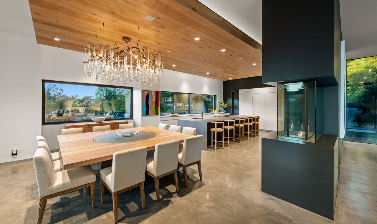 Above the dining area, a sculptural chandelier crafted from twisted branches and crystals hangs over the large wood dining table, surrounded by white cushioned chairs.