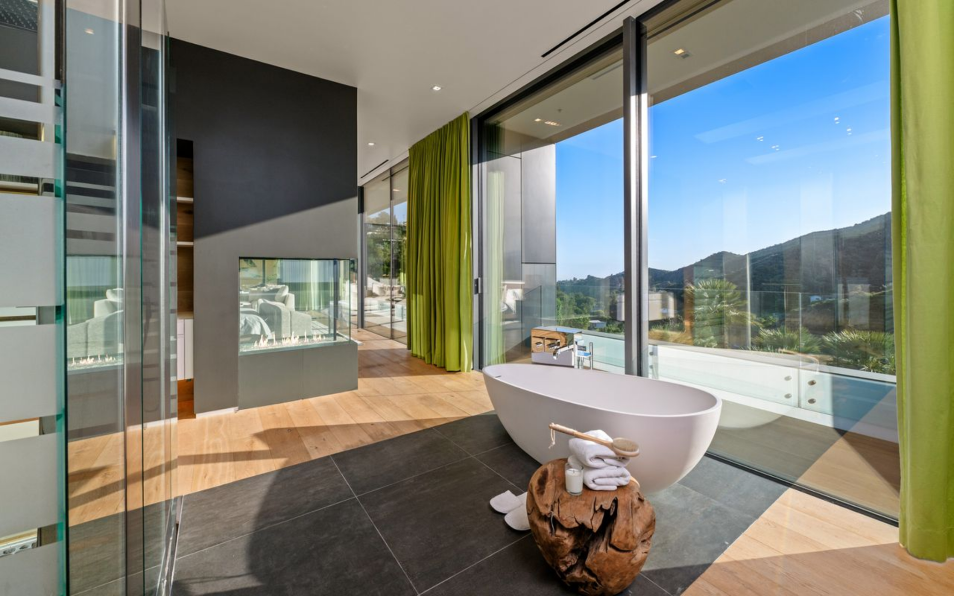Inside, a freestanding soaking tub is placed beside the windows, with a glass-enclosed shower, dark stone flooring, and clean-lined finishes giving the space a polished, contemporary look.