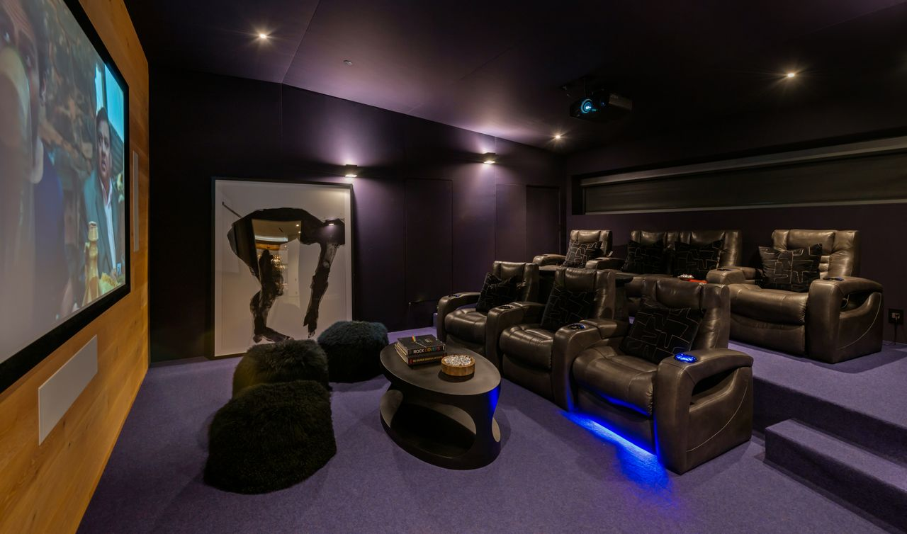 The home theater is set up as a dedicated screening room, with dark walls, a large projection screen, and tiered seating.