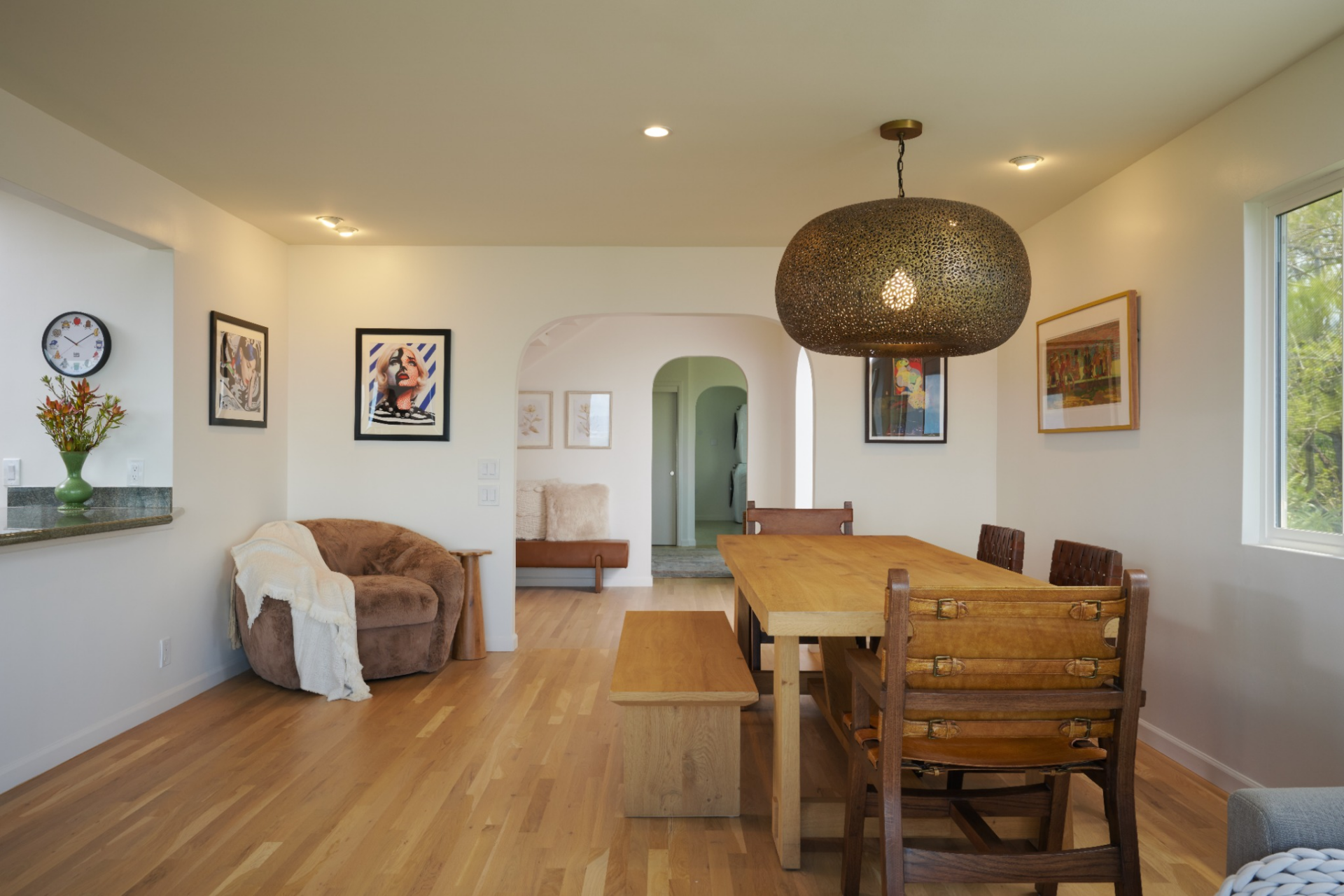 White oak floors run throughout, while a large pendant light anchors the wood dining table before the room continues into a sitting area framed by wide windows and sliding glass doors.