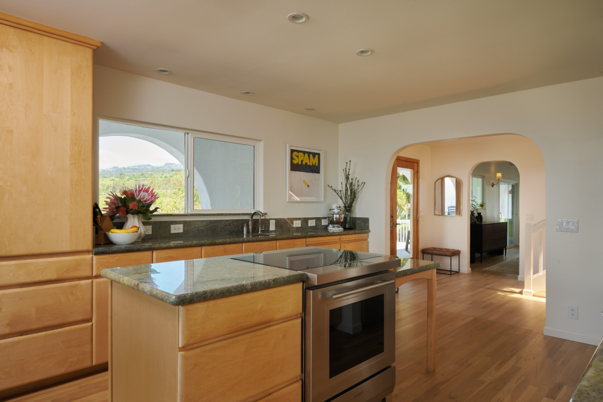 The kitchen sits just beside these open spaces, connected through a wide passage and finished with light wood cabinetry, stone counters, and Wolf appliances.