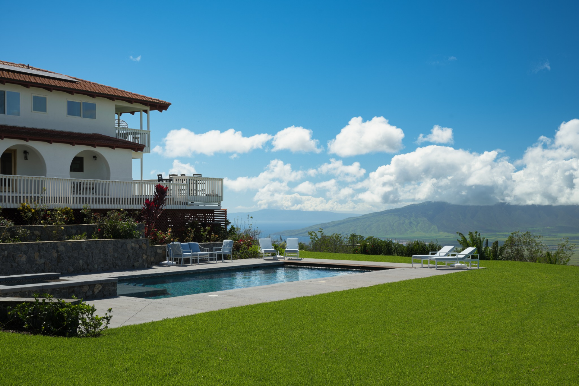 The main yard unfolds from the home with a broad lawn and a 40-foot saltwater pool and spa set into a clean concrete surround, creating a central gathering point against the backdrop of the ocean and mountains.
