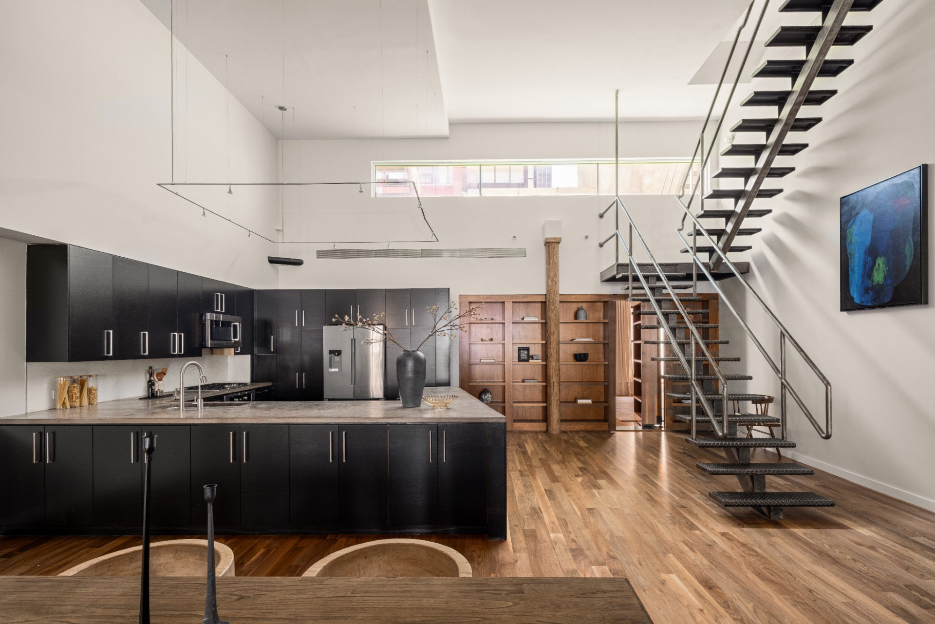 Dark cabinetry runs along the back wall and wraps around a large central island topped in concrete, while stainless-steel appliances are integrated throughout.