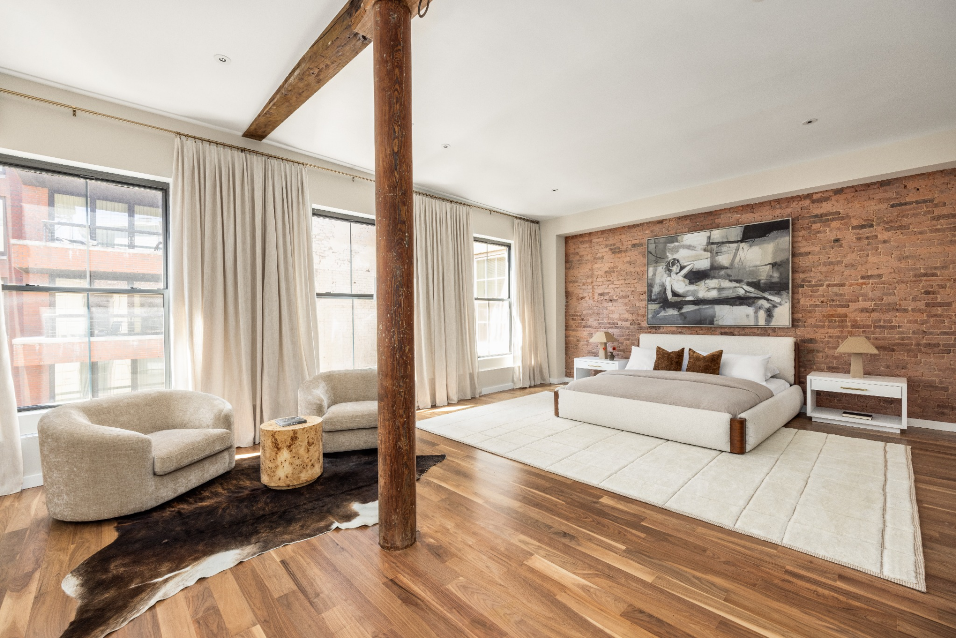 Inside, the space opens wide with the same exposed brick and timber elements, softened by a low-profile bed, neutral textiles, and a seating area positioned near the windows.