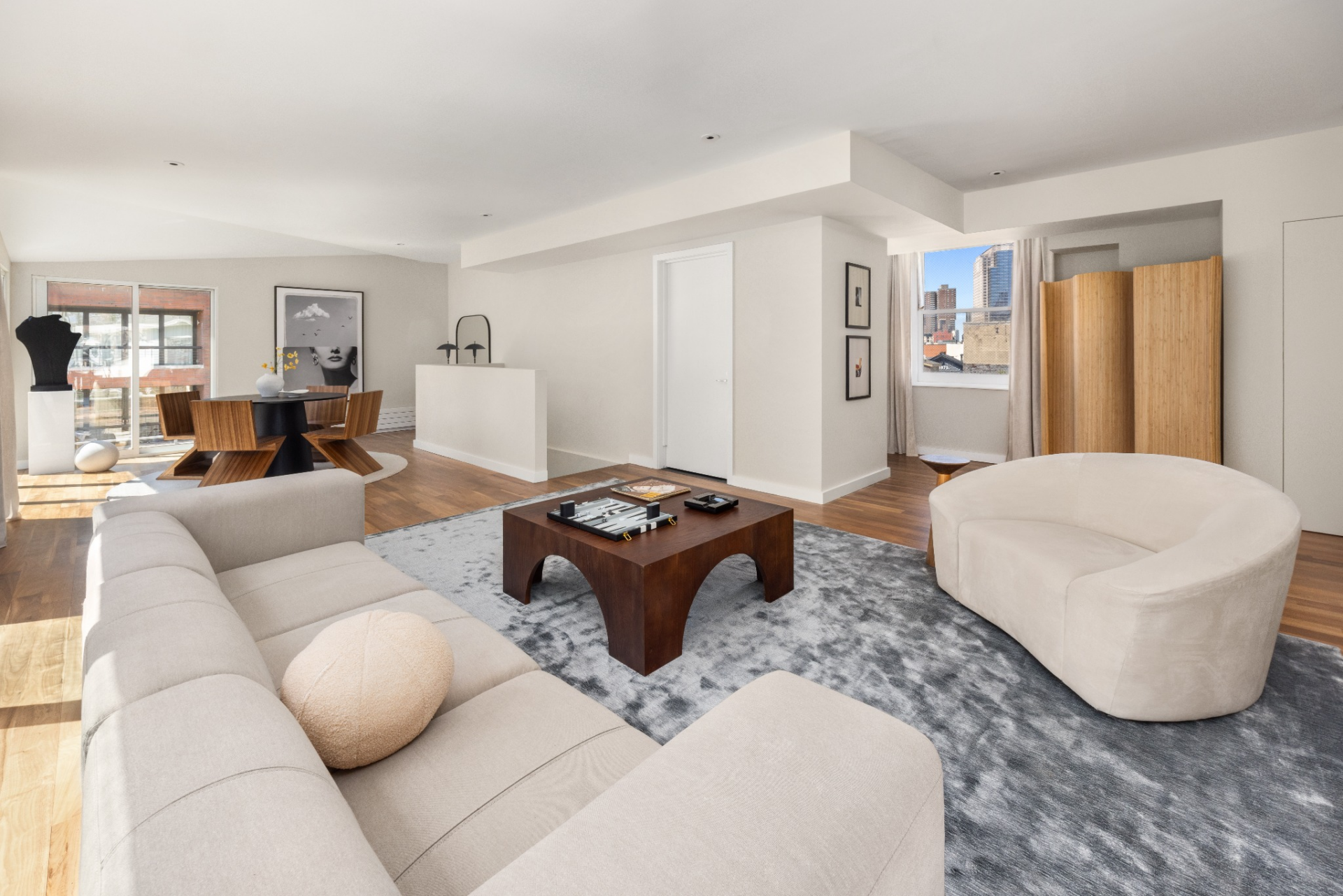 The layout opens into a lounge setup with low-profile seating arranged around a central coffee table, while a dining area sits just beyond near the windows.