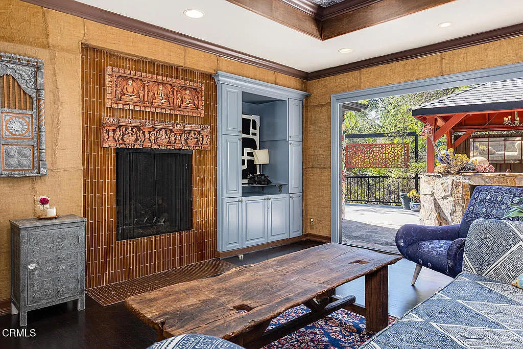 The room itself sits between a built-in wood bookcase that stretches across the back wall and a brown tile-lined fireplace with carved pieces.