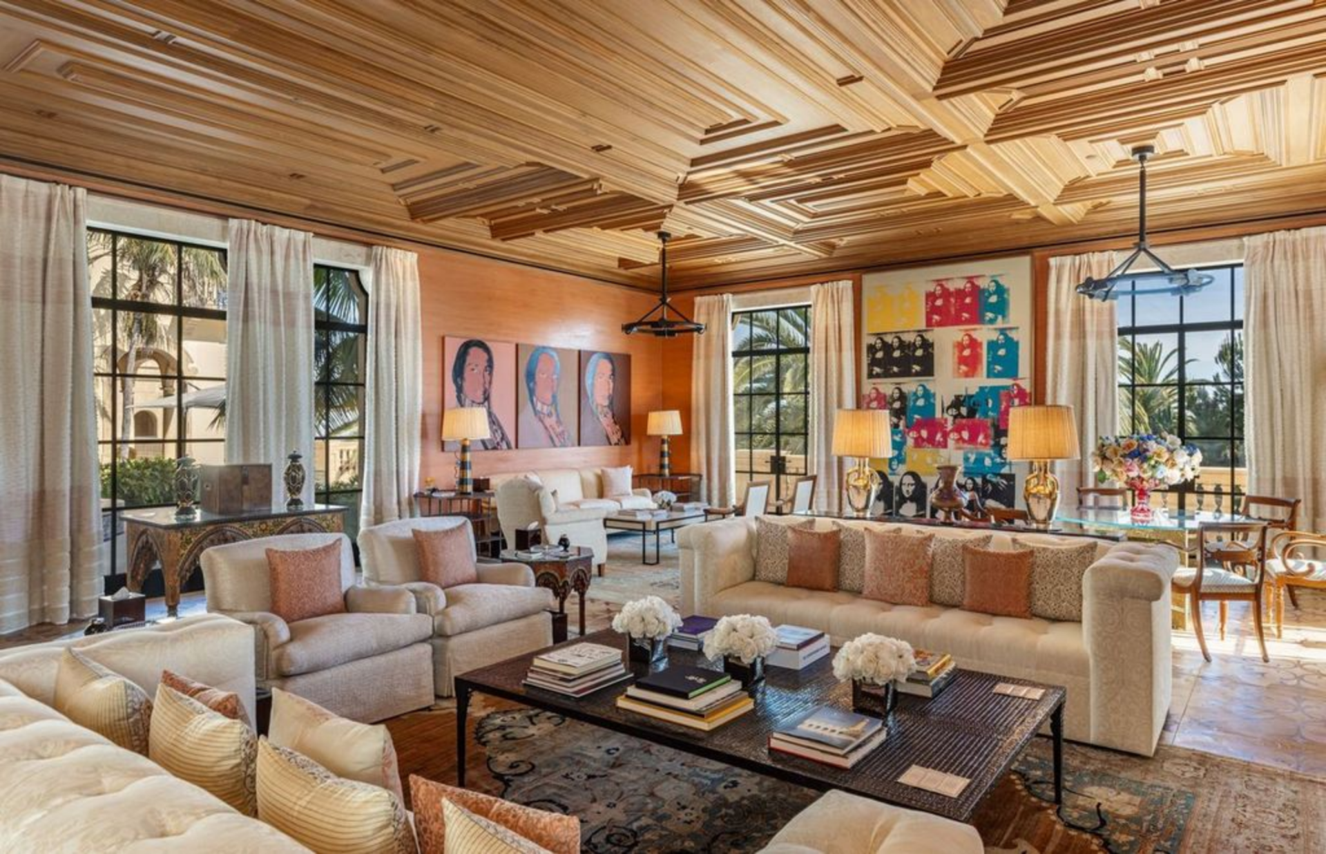 Seating is arranged in multiple groupings, with sofas and armchairs centered around a large coffee table, while walls are lined with bold, gallery-style artwork that anchors the space visually. 