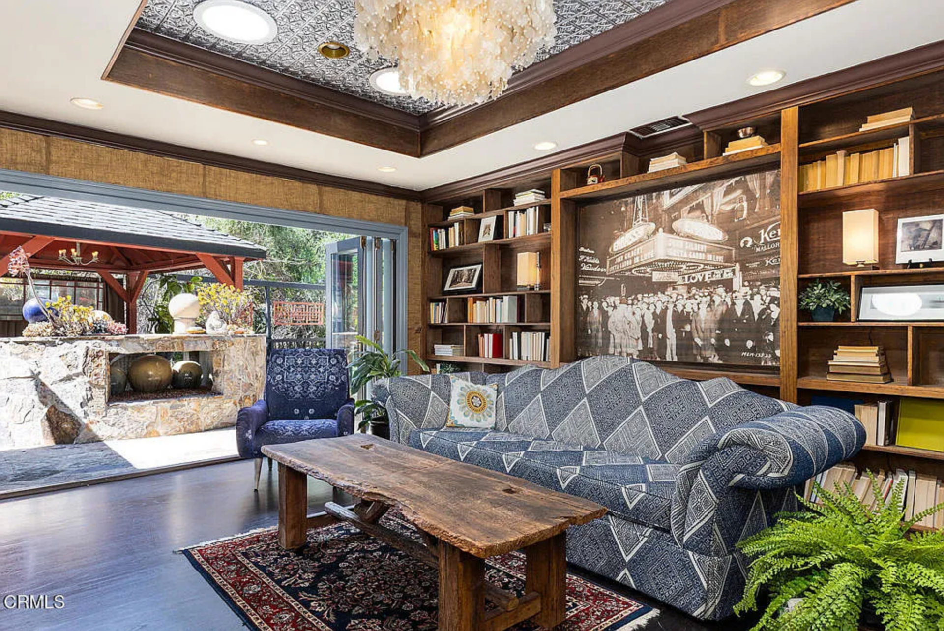 Overhead, the tin ceiling sits inside a recessed wood-trimmed border and draws the eye up to a layered chandelier, while below, a patterned sofa, rustic wood coffee table, and dark flooring keep the room grounded.