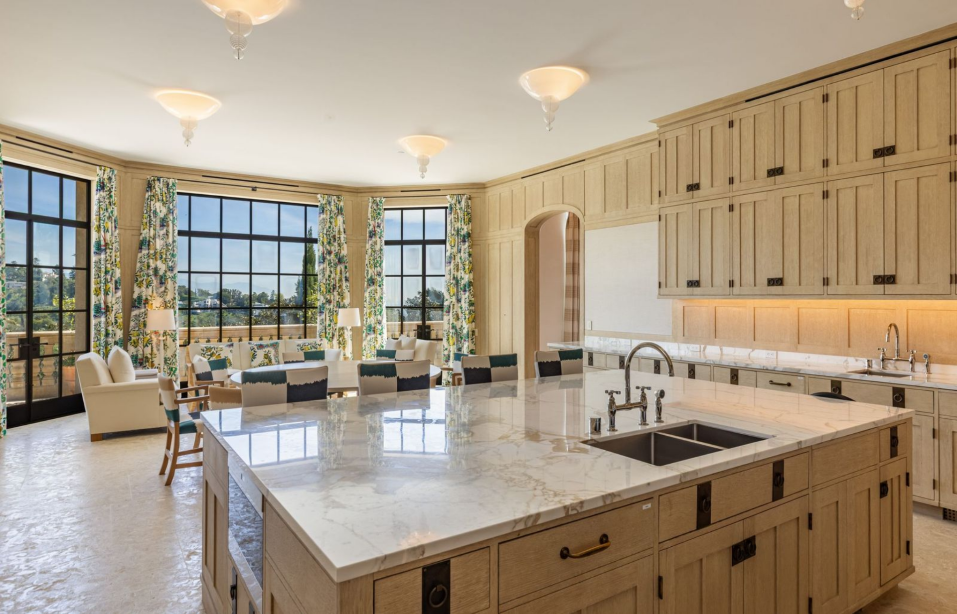 The family kitchen continues the main residence’s light, tailored palette, with pale wood cabinetry wrapping the walls and a large marble-topped island in the center of the room.