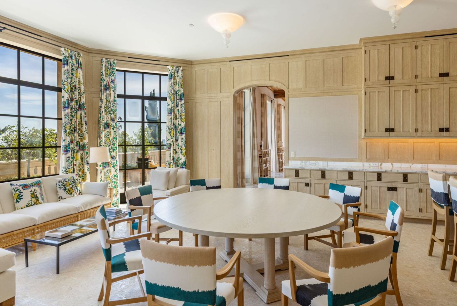 A round table sits at the center, with upholstered chairs and a nearby sofa creating a more relaxed everyday gathering area against the windows.