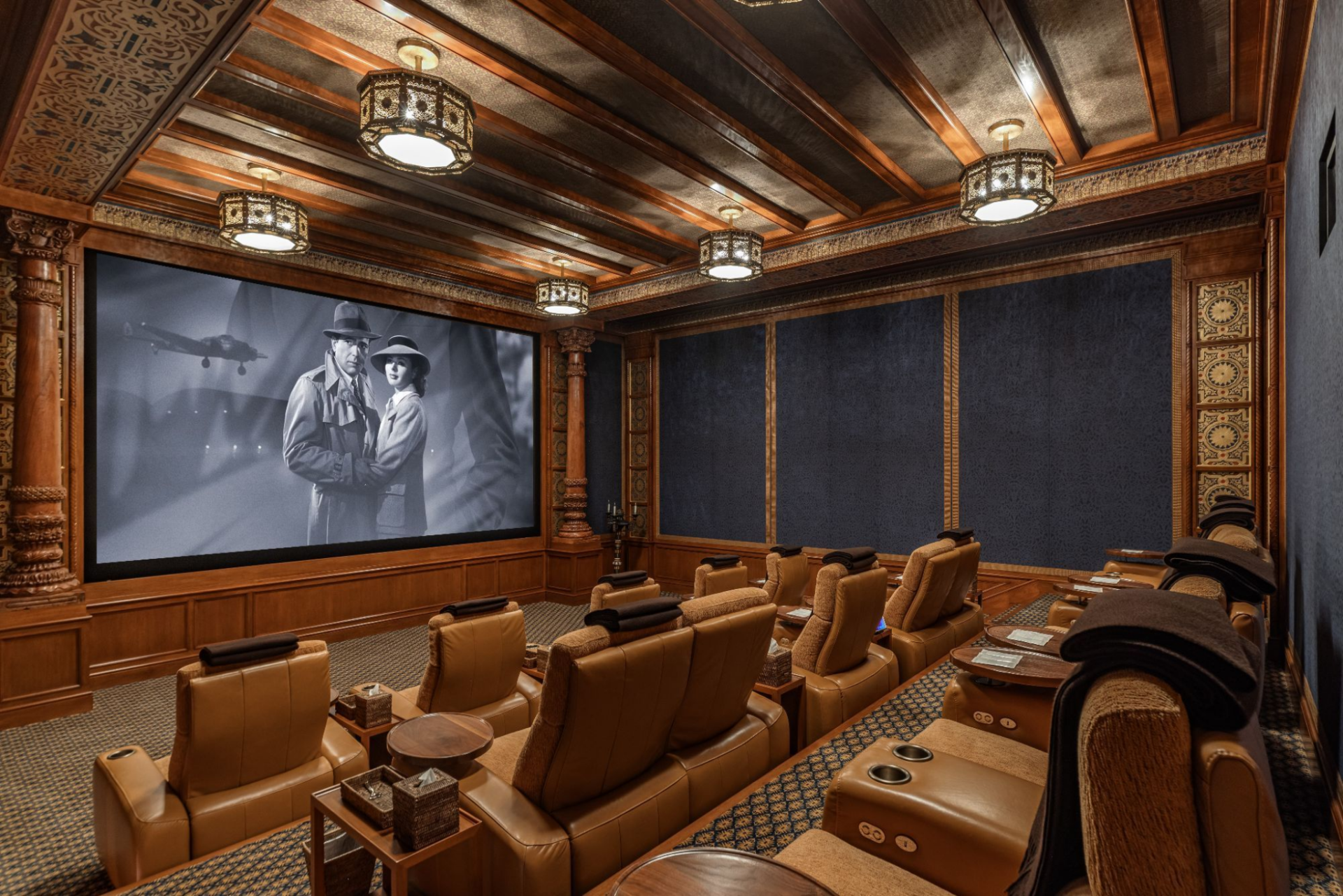 The movie theater is finished with carved wood paneling, patterned wall panels, and rows of leather recliners. 