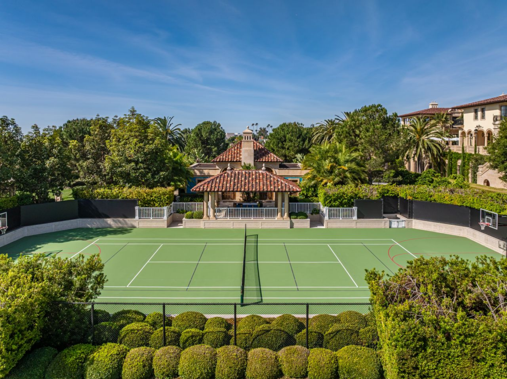 Set off to the side of the property, the tennis court is enclosed by hedges and fencing, with the pool house sitting right at the center of the court.