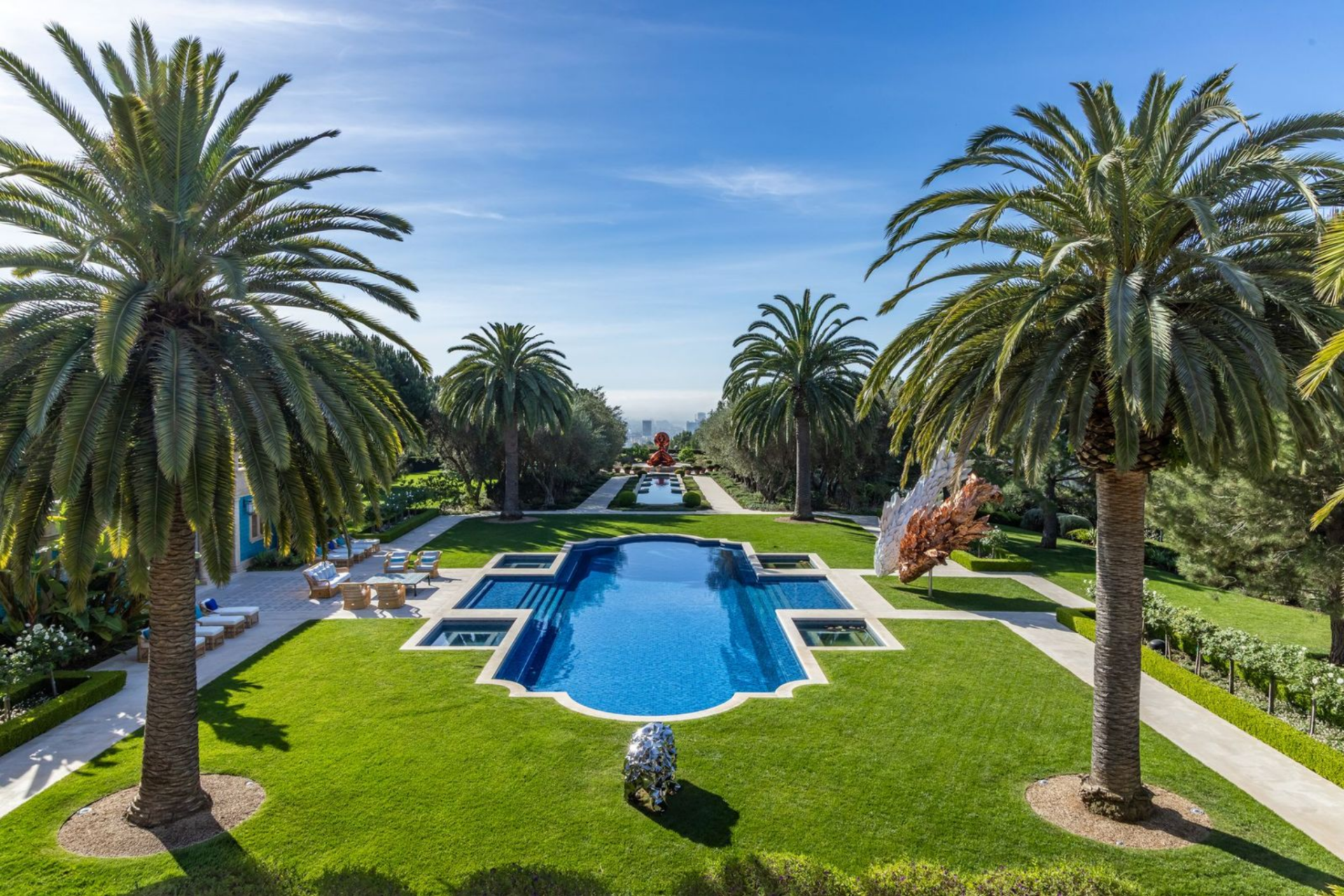 At the center of the backyard, the main pool is framed by palm trees with a geometric shape that mirrors the symmetry of the grounds. 