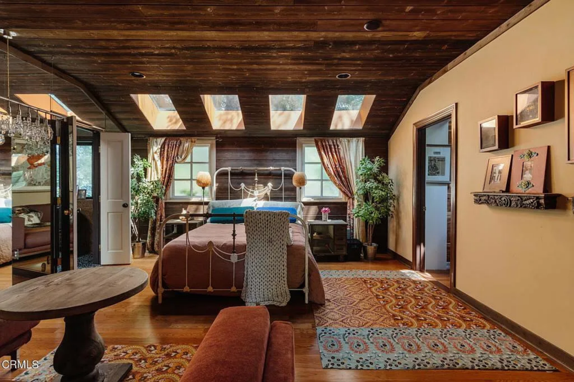 Down the hall, the primary suite begins with the bedroom opening out beneath a dark wood plank ceiling lined with skylights sitting above the bed.