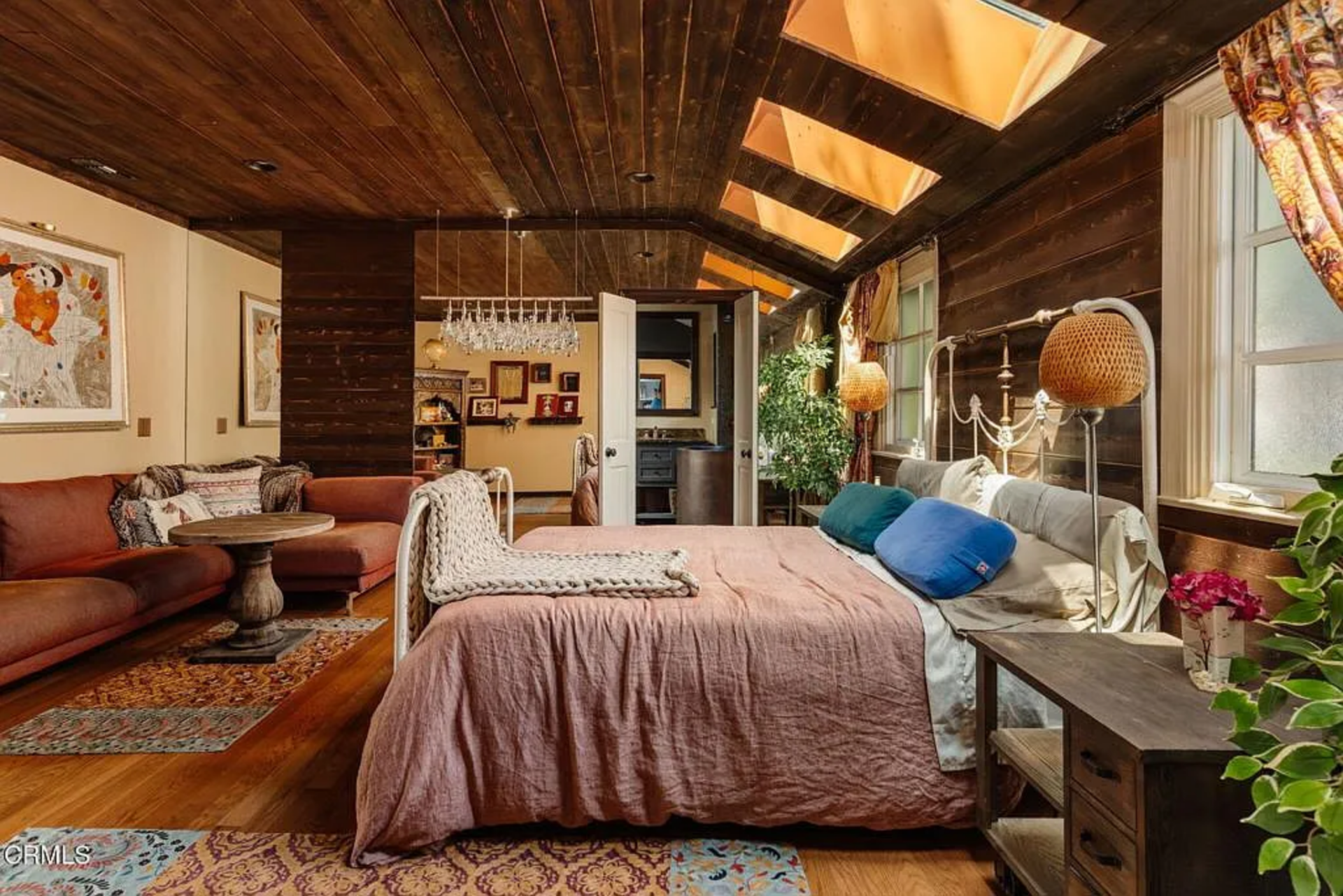From there, the room stretches beyond the sleeping area into a sitting space with a rust-colored sectional, patterned rugs, and warm wood floors.