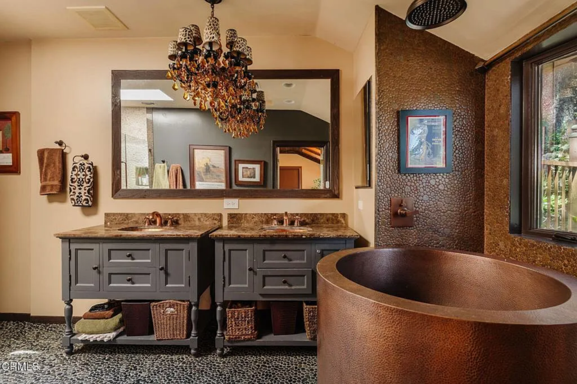 Through the open white doors, the en-suite bathroom has a hammered copper soaking tub, pebble flooring, textured walls, and a long double vanity with dark cabinetry.