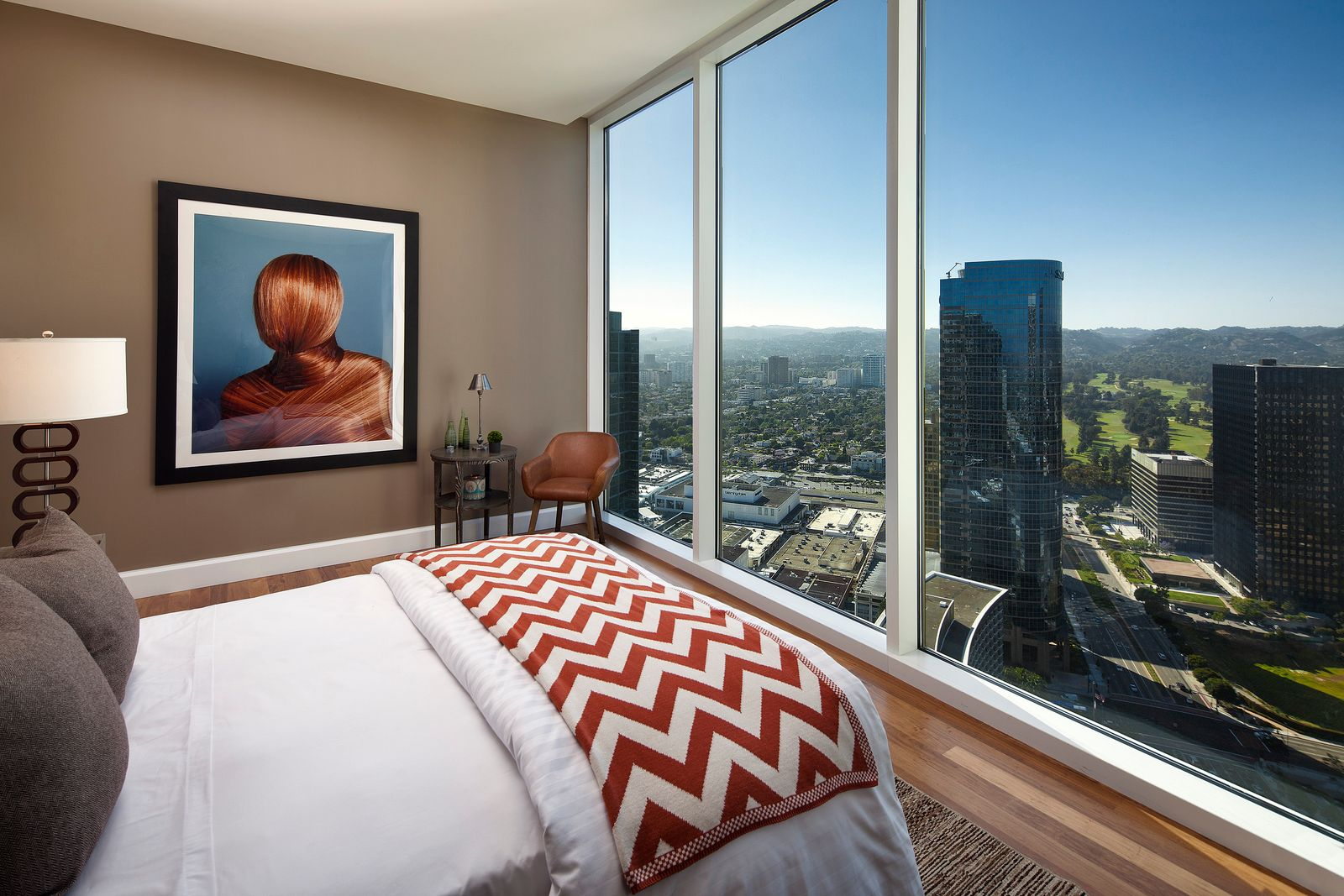 Lastly, one of the guest bedrooms' beds is positioned to face floor-to-ceiling glass, turning the skyline views into the room’s main design feature, while warm wood floors and taupe walls keep the space grounded.