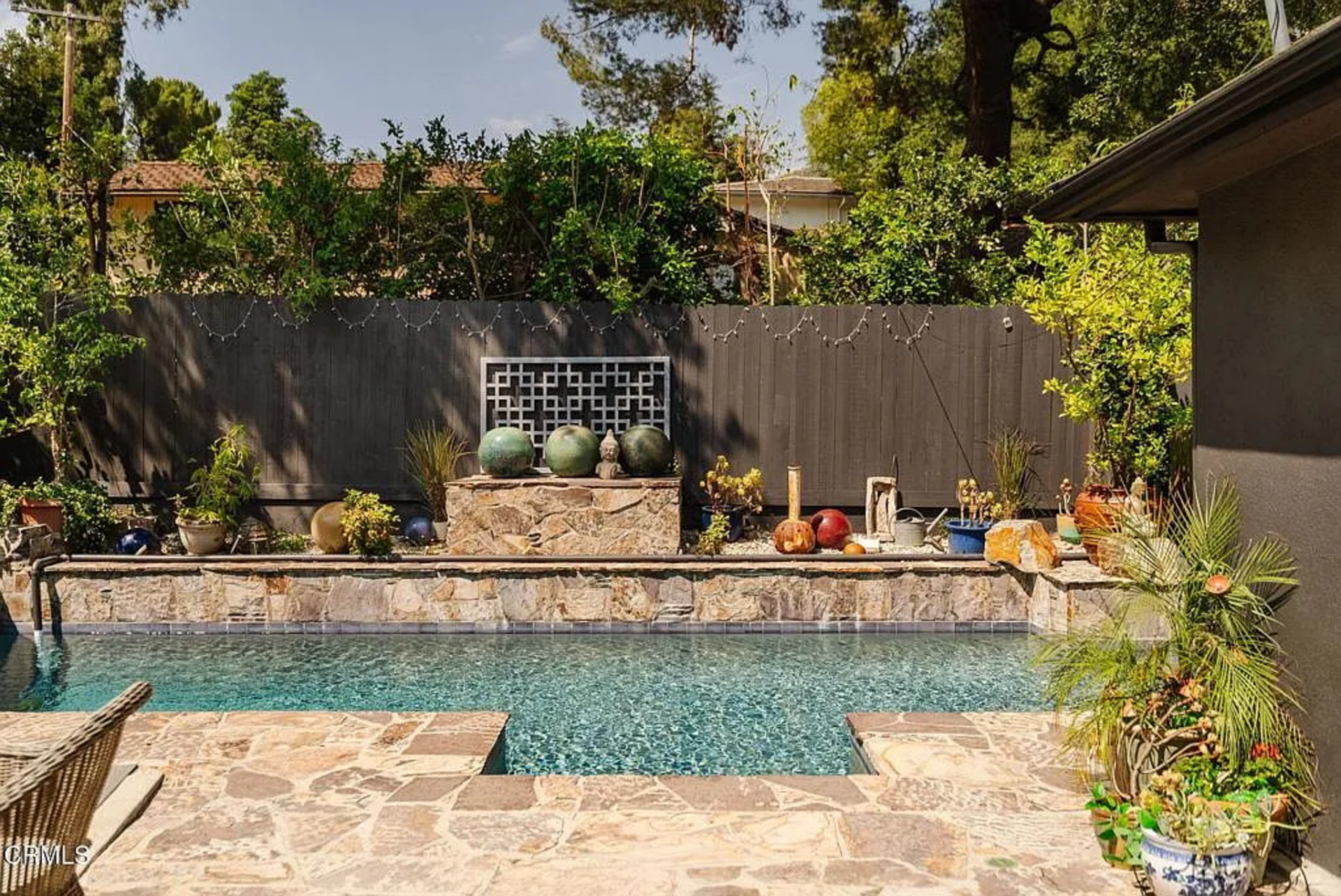 On the other side of the yard, the pool is set into a stone surround with a raised wall running along the back, lined with planters and decorative pieces.