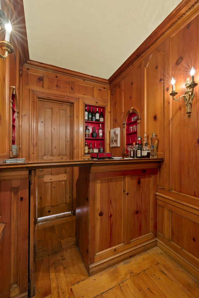 Once opened, the room shifts from the pale palette of the library to a much darker wood-lined interior, with a compact serving counter and shelves inset with bottles and glassware, preserving a rare piece of the home’s original entertaining history.