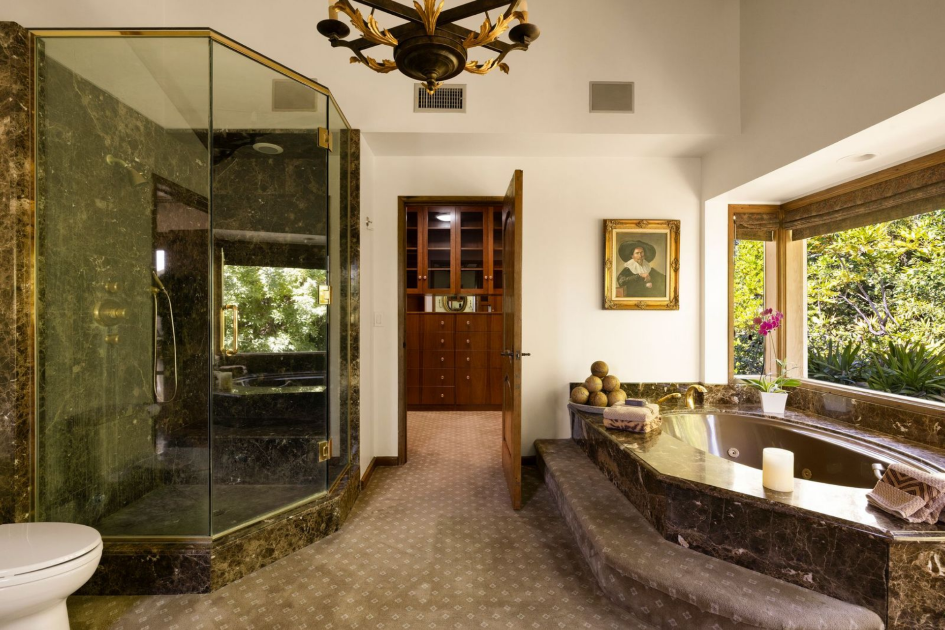 The other is brighter with a glass-enclosed shower, a deep jetted tub set into dark stone beneath the windows, and direct access to a custom closet.