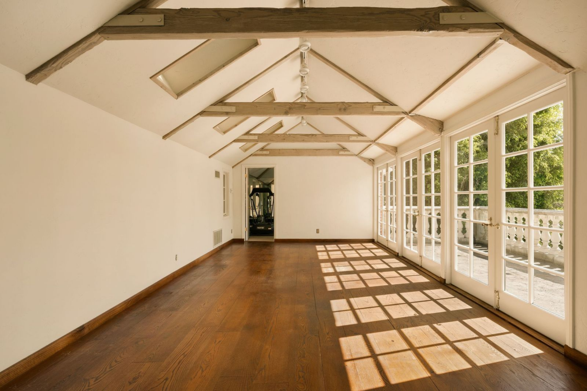 Upstairs, the guest house shifts into a long open room beneath a pitched ceiling with exposed trusses and a full row of French doors lining one side. 