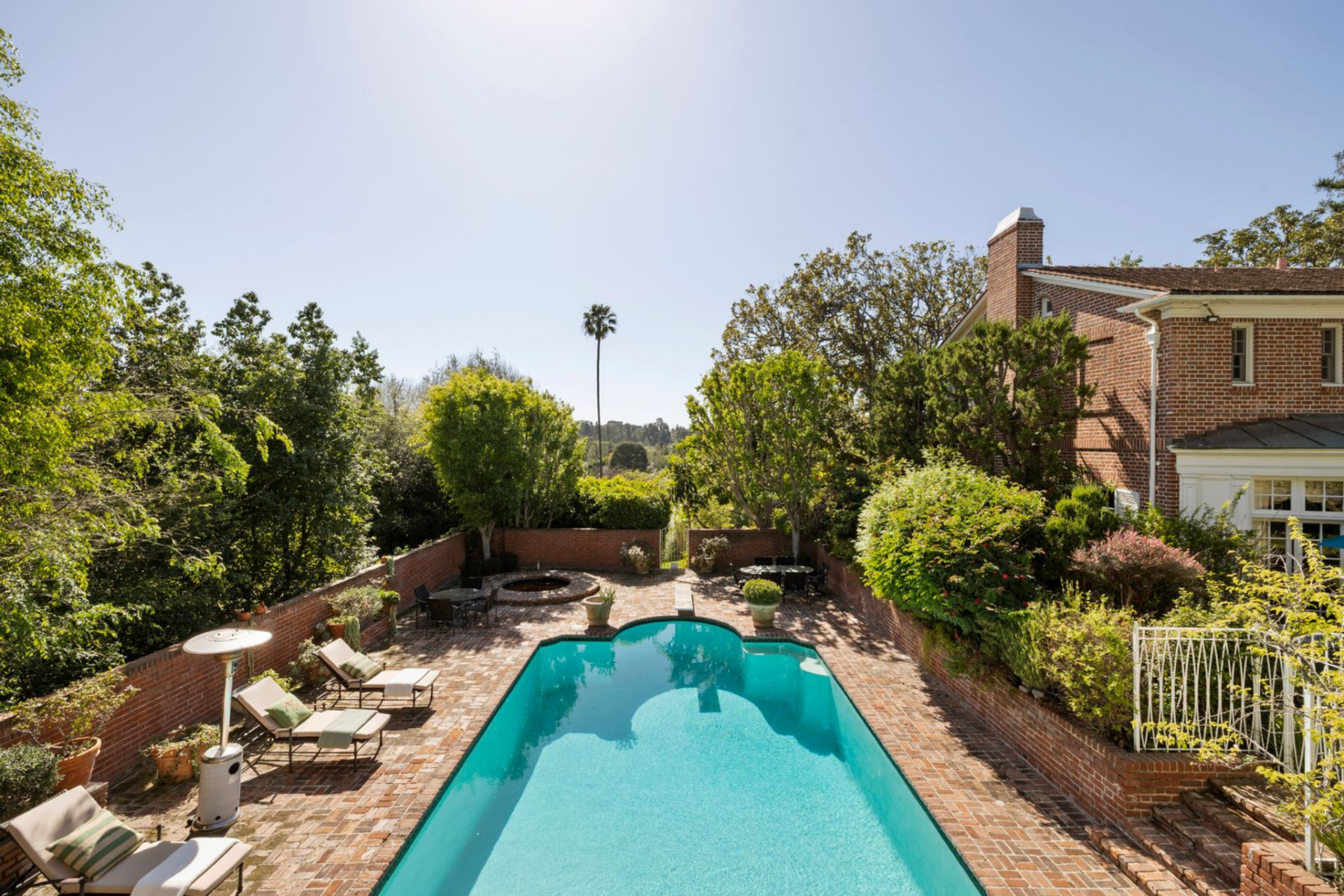The pool sits within a brick terrace behind the house, with clipped plants and raised brick walls framing the space on all sides. 