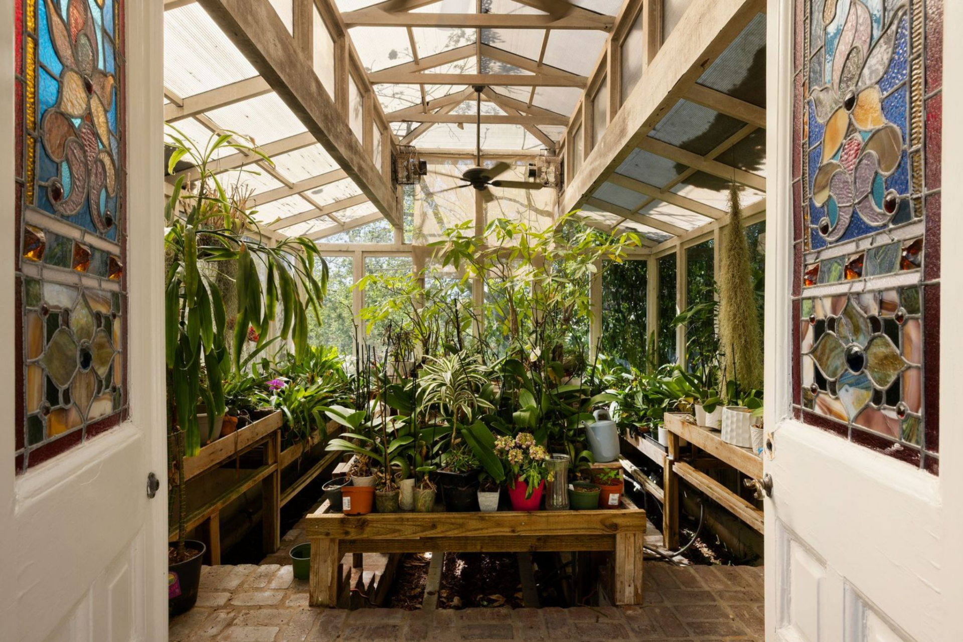 Inside, the structure is fitted with long planting tables and stained-glass doors, giving it the look of a working greenhouse rather than a decorative garden room.