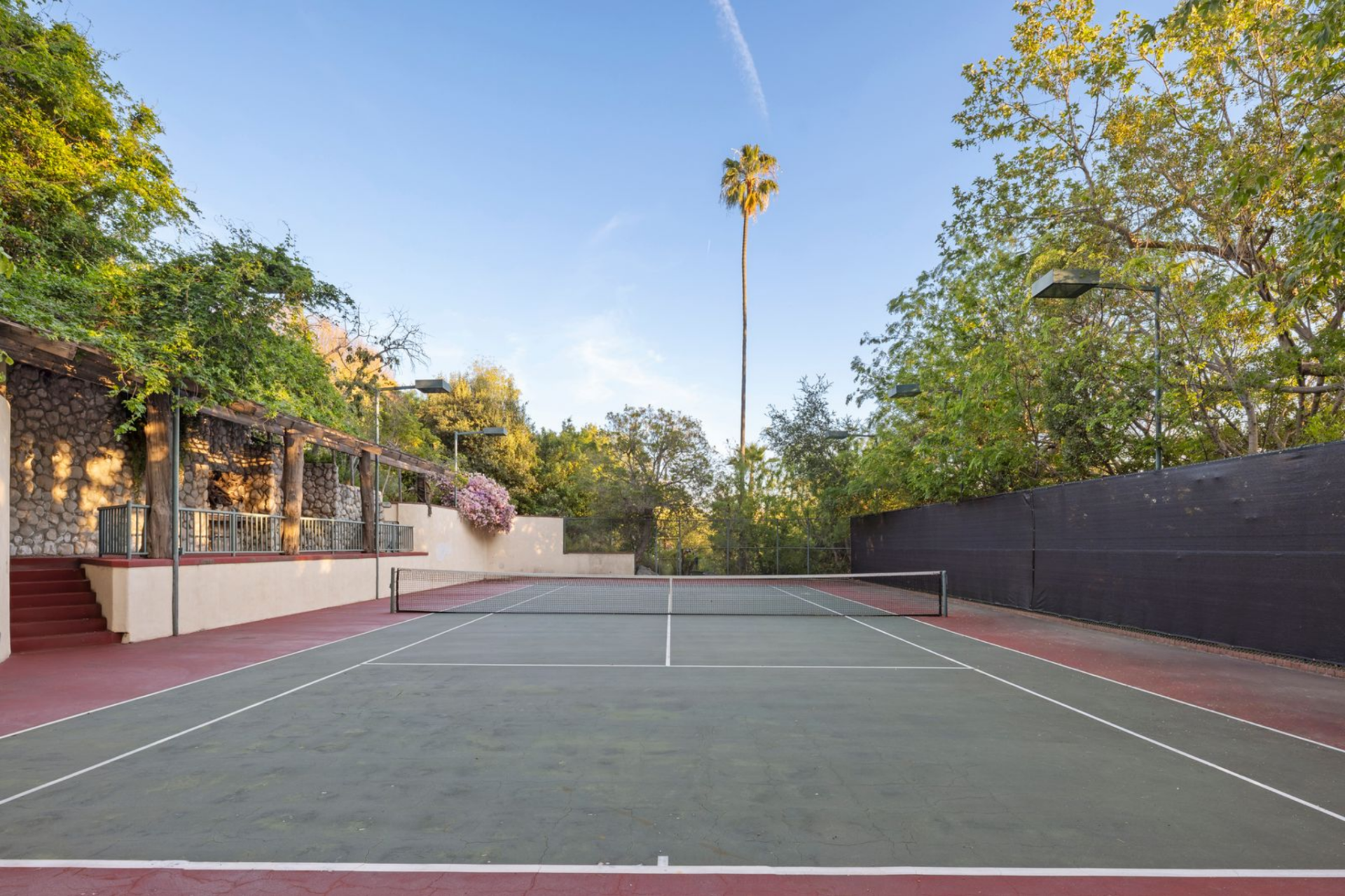 A full-size tennis court occupies another section of the grounds, set below retaining walls and surrounded by thick trees that keep it screened from the rest of the property.