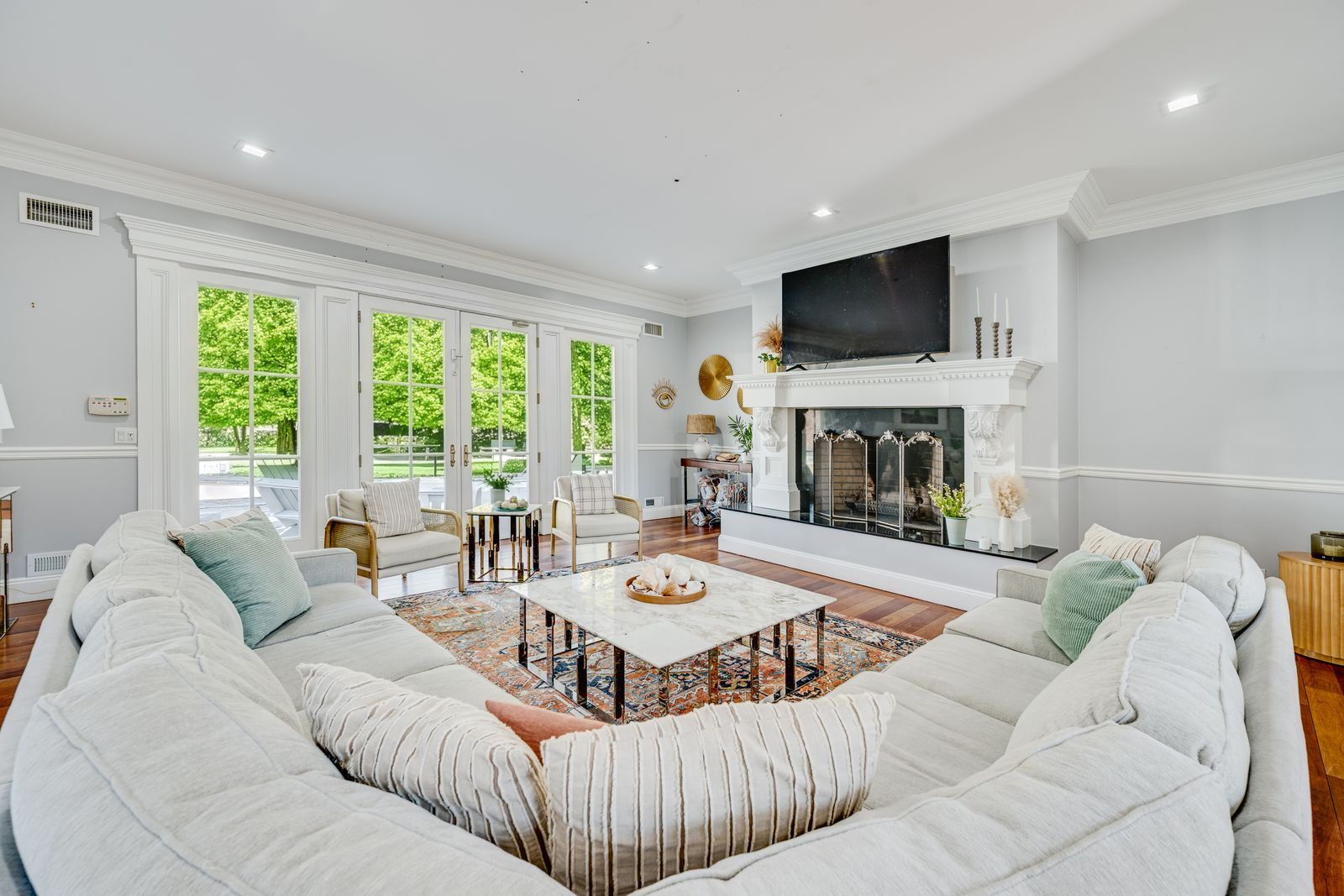 Detailed millwork frames the room from the crown molding to the paneled walls and carved fireplace surround, while wide-plank hardwood adds warmth beneath the lighter furnishings.